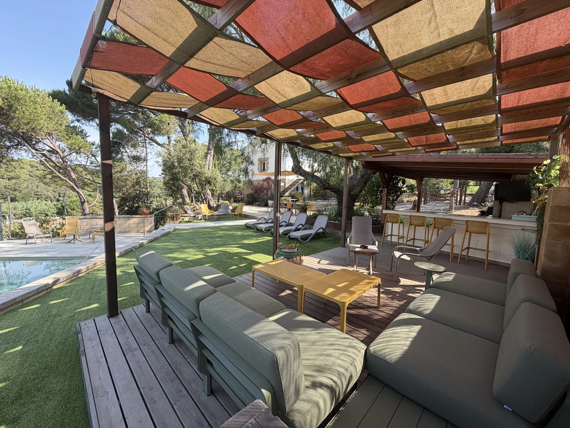 Los sofás del chillout bajo la pérgola, con el césped y la barra al fondo