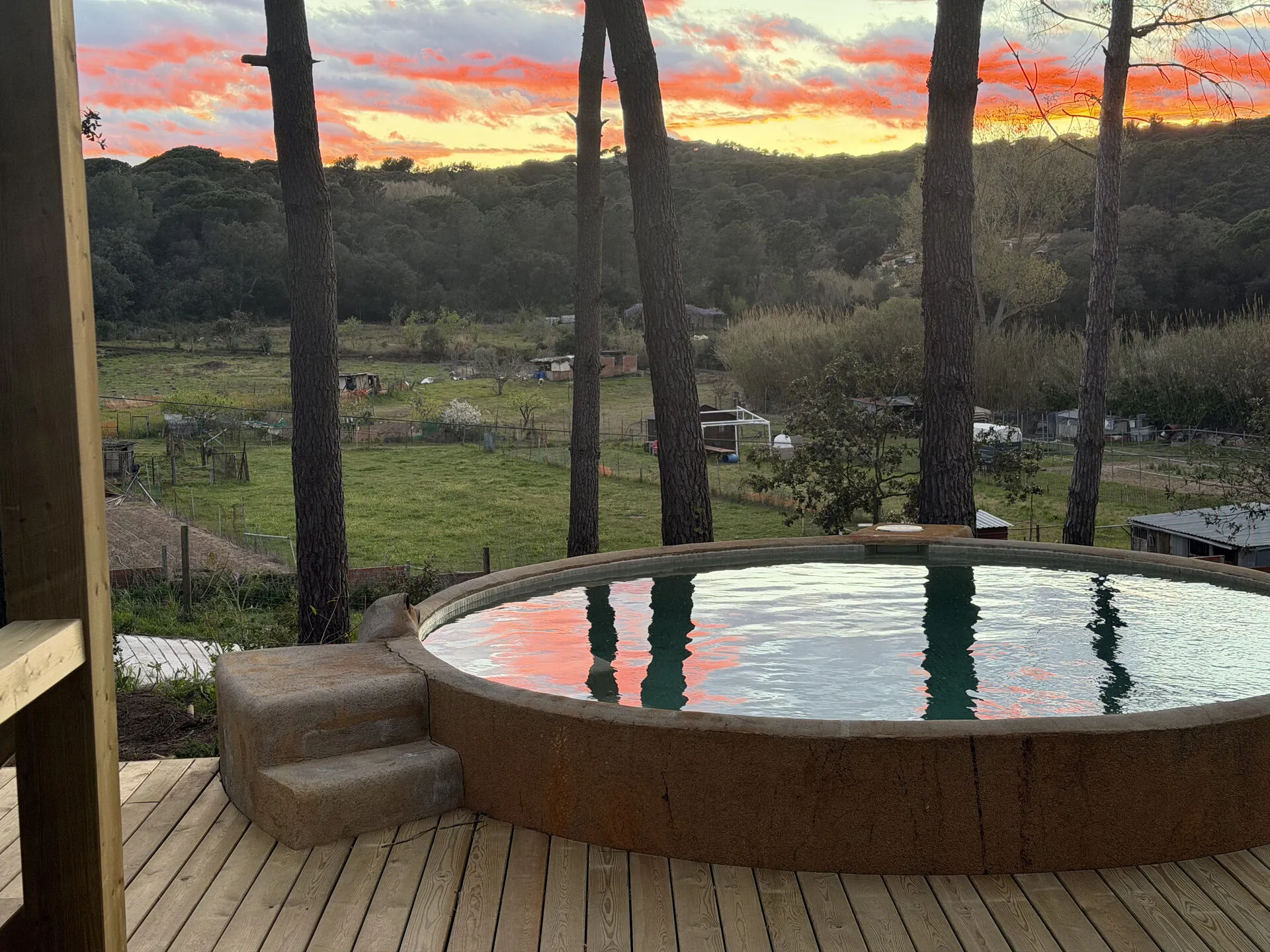 La piscina redonda reflejando el atardecer, en la terraza chillout de madera